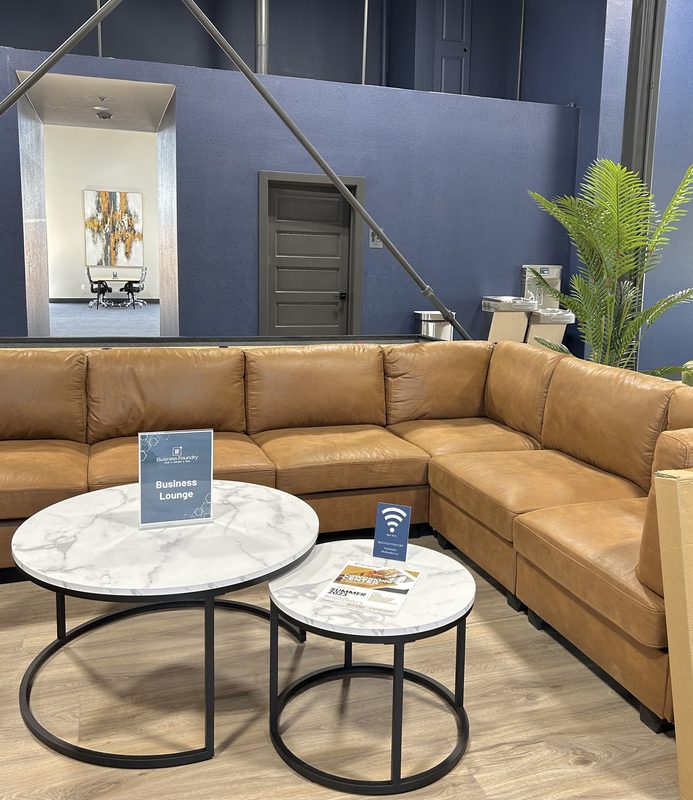 The business lounge: a tan leather sectional around two marble tables, with the room’s own Business Lounge sign on one of them