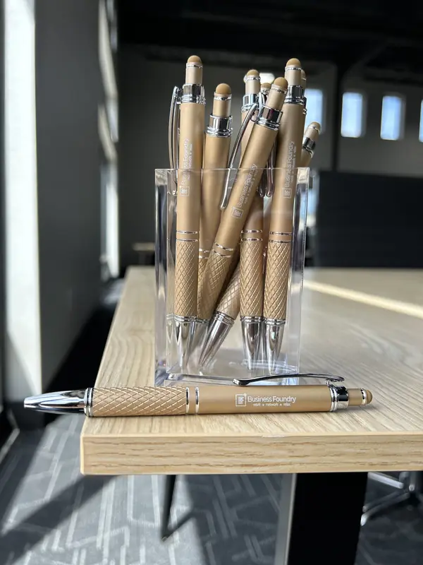 Business Foundry branded pens in a holder on a light wood meeting room table