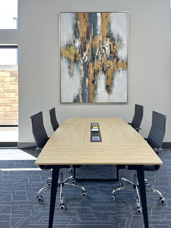 A light wood meeting table with black chairs down both sides, one of several tables in the open meeting room