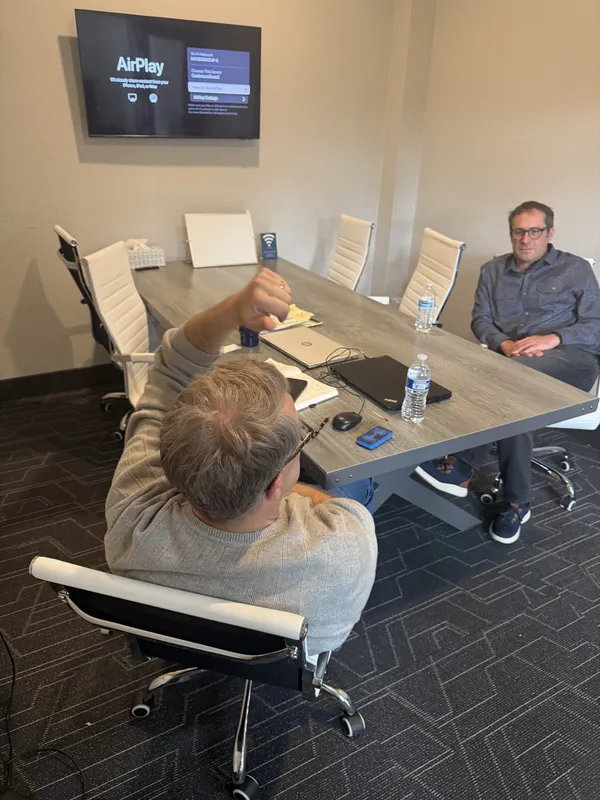 A closer view across the conference table, laptops and water bottles out, the wall screen above