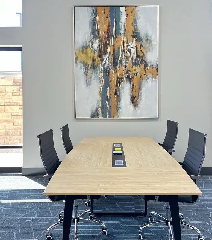 A light wood meeting table with black mesh chairs down both sides, power sockets set into the centre and a painting on the wall behind it