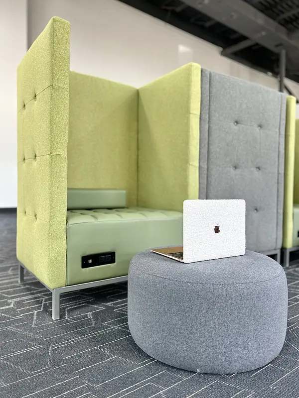 An open work booth with a power socket built into the upholstered seat and a laptop resting on a round stool