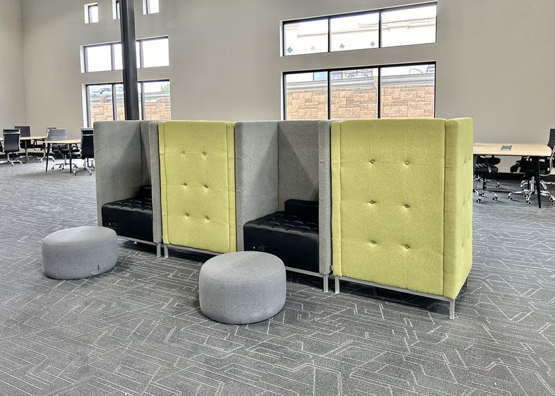 A row of high-backed lime green coworking booths with grey ottomans