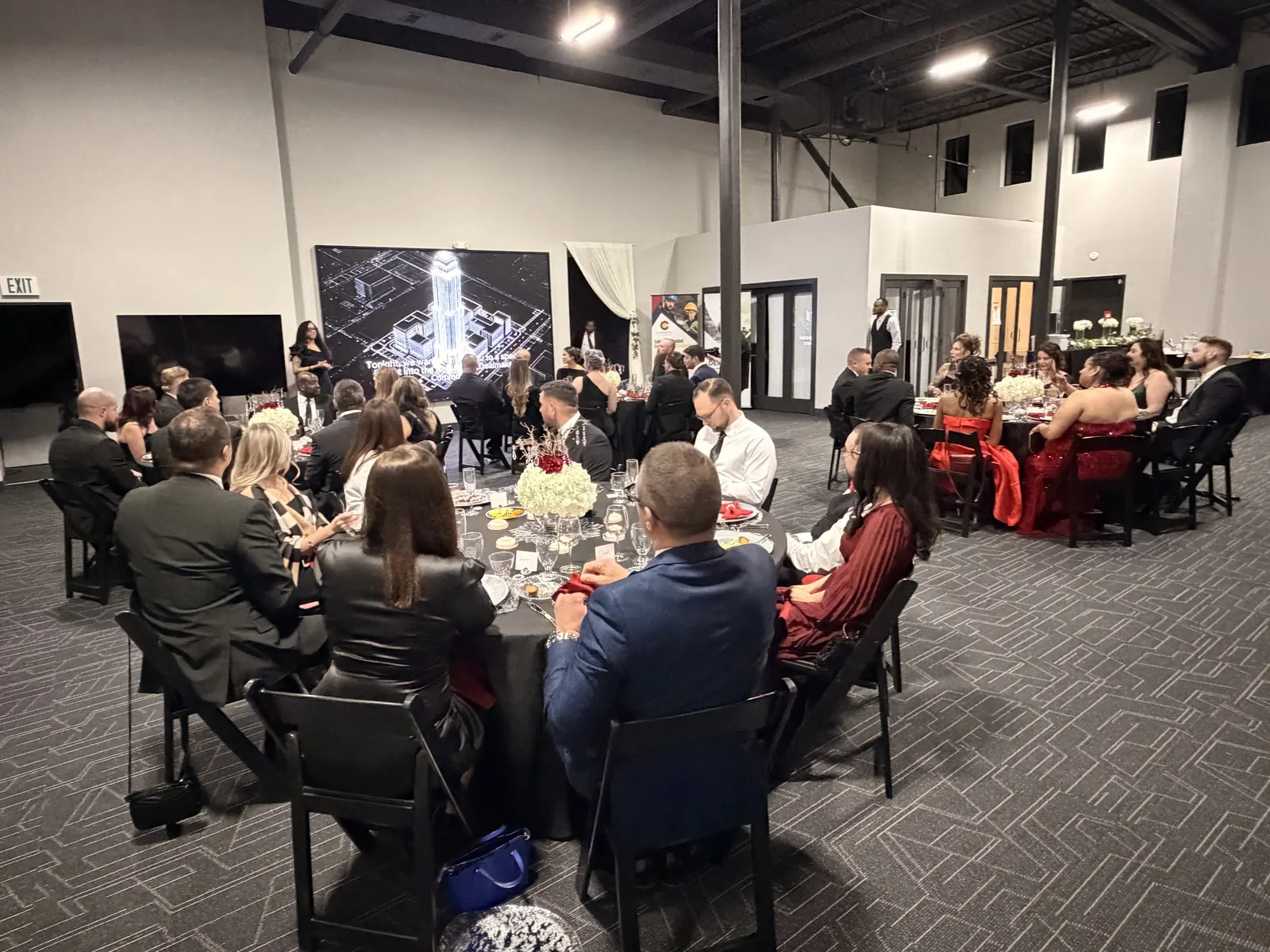 A black-tie dinner on the event floor, guests in evening dress at round tables set with white flowers
