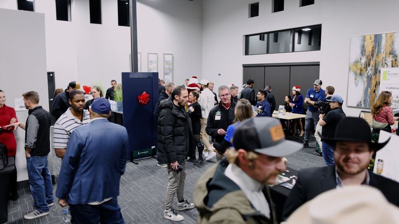 A crowded holiday networking mixer, guests talking between vendor tables