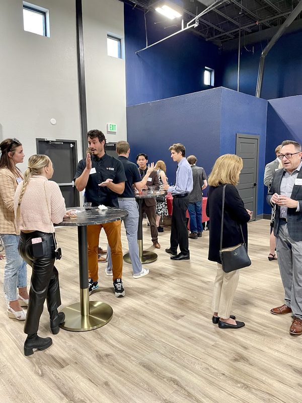 A standing crowd talking in small groups at high tables on the ground-level event floor