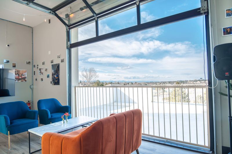 A garage door rolled up to the balcony railing and a wide Colorado sky, with blue armchairs and an orange sofa in front