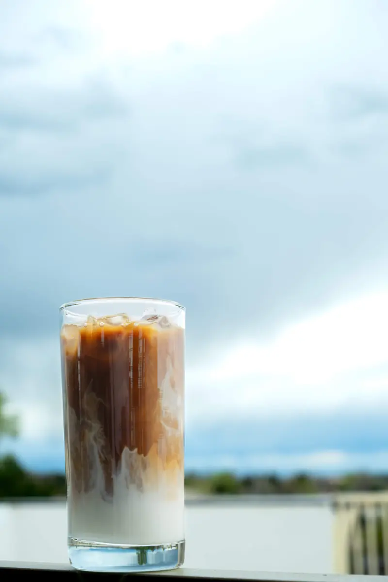 An iced latte on a ledge against a cloudy sky