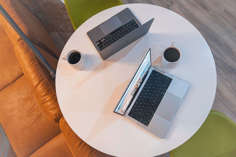 Two laptops and two coffees on a round white table, seen from above