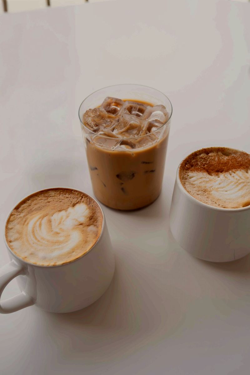 Two lattes with leaf art beside an iced coffee
