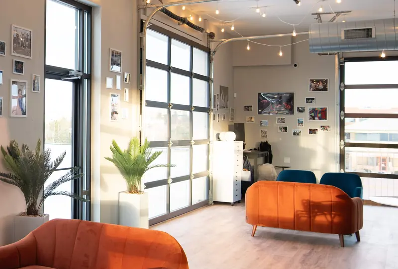 Afternoon light on an orange sofa under string lights, with potted palms by the windows
