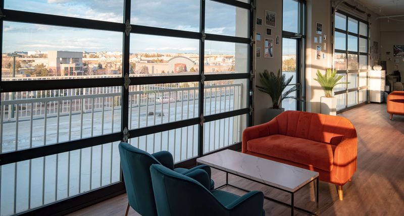 An orange sofa and teal armchairs in afternoon sun beside the garage-door windows
