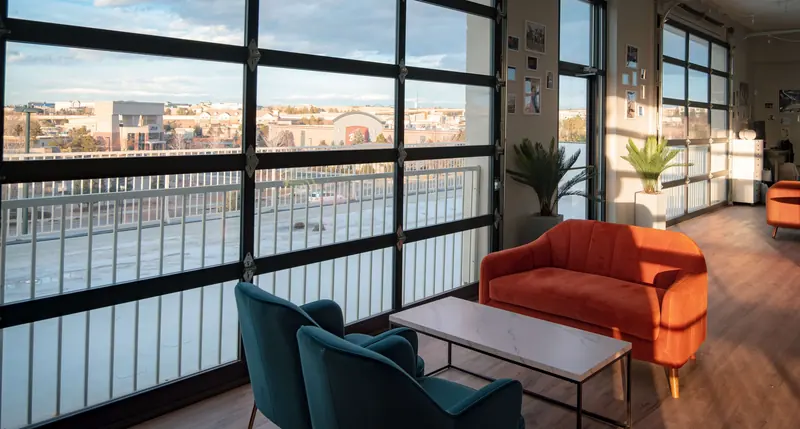 An orange sofa and teal armchairs in afternoon sun beside the garage-door windows