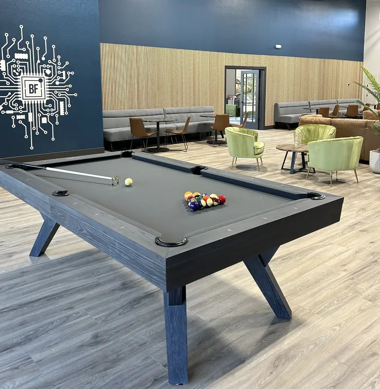 The lounge pool table in front of the circuit-board mural, with banquette seating, green velvet chairs and the glass entrance beyond