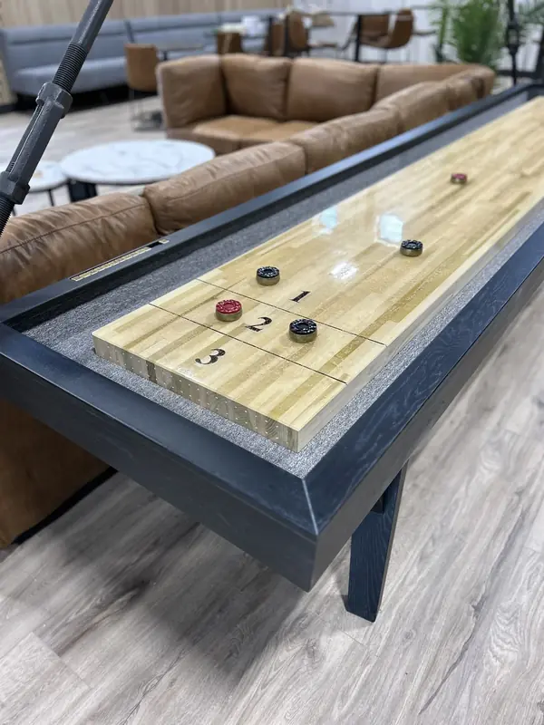 The shuffleboard table in the lounge, its pucks mid-game, with leather sofas and marble tables behind it
